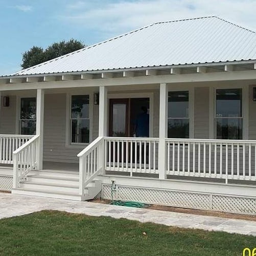 White coastal home with wraparound porch and metal roof