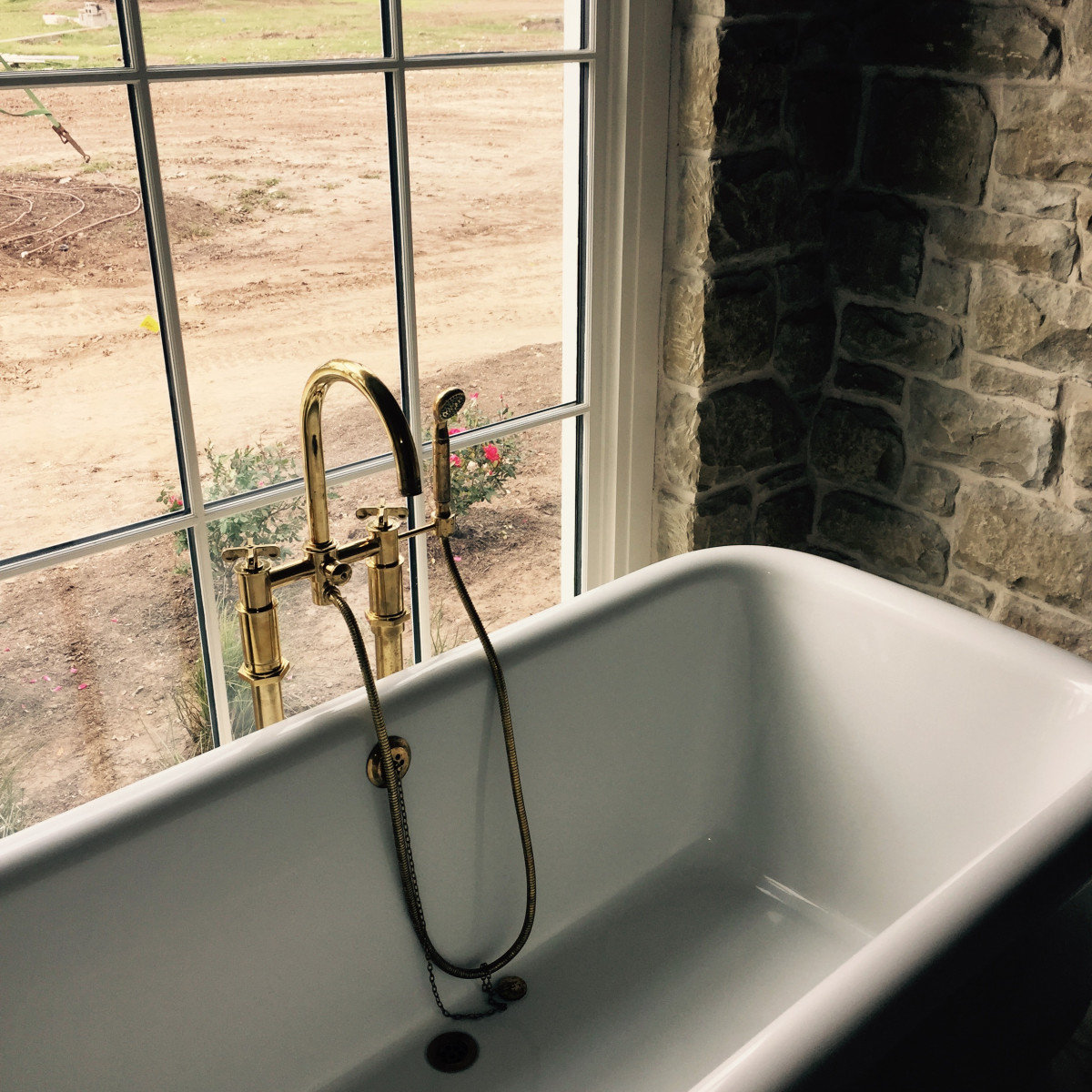 Freestanding tub with brass fixtures and stone wall