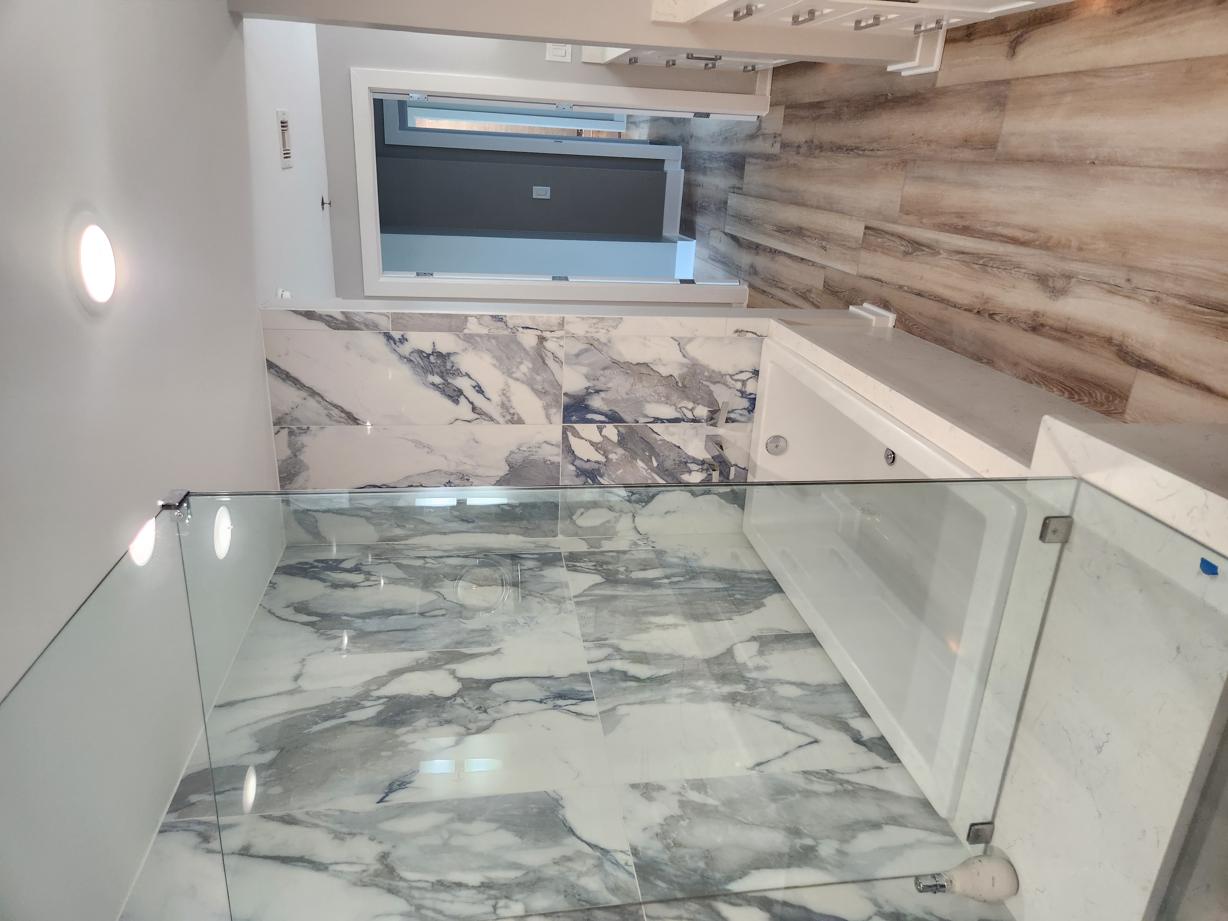Marble bathroom with glass shower and wood accent wall