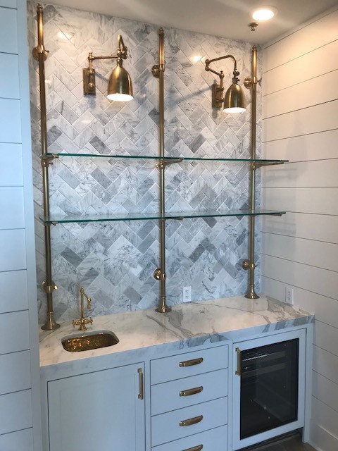 Wet bar with herringbone marble backsplash and brass fixtures
