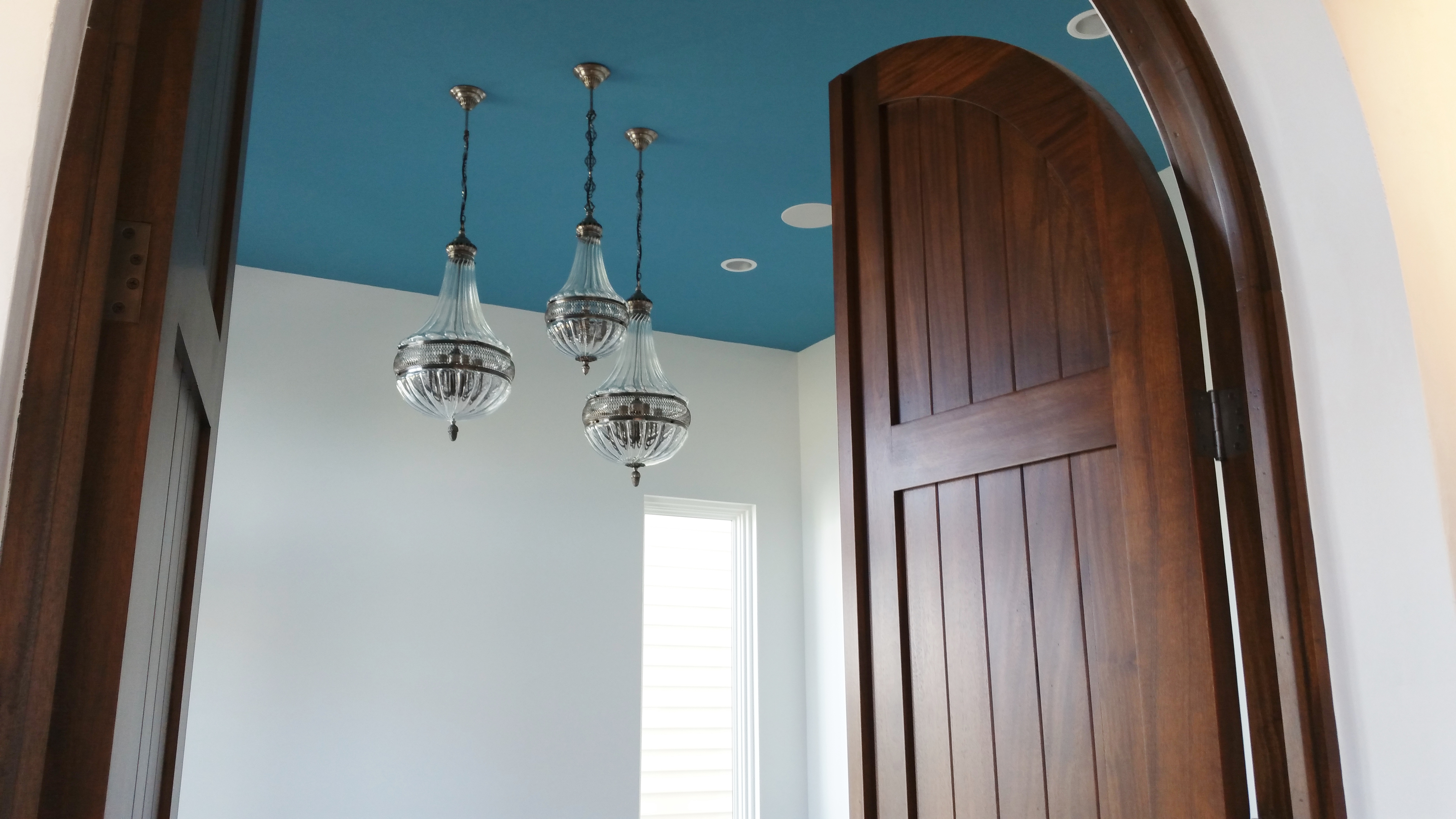 Arched mahogany doorway with teal ceiling and chandeliers